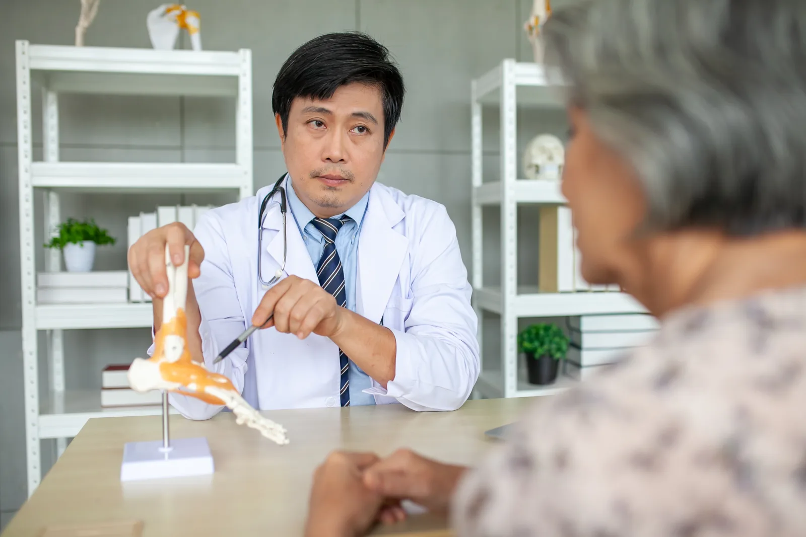 Doctor explaining foot pain to an older patient using an anatomical model